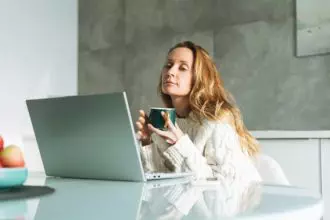 Young adult blonde woman with long hair working on laptop on kitchen at home, remote work